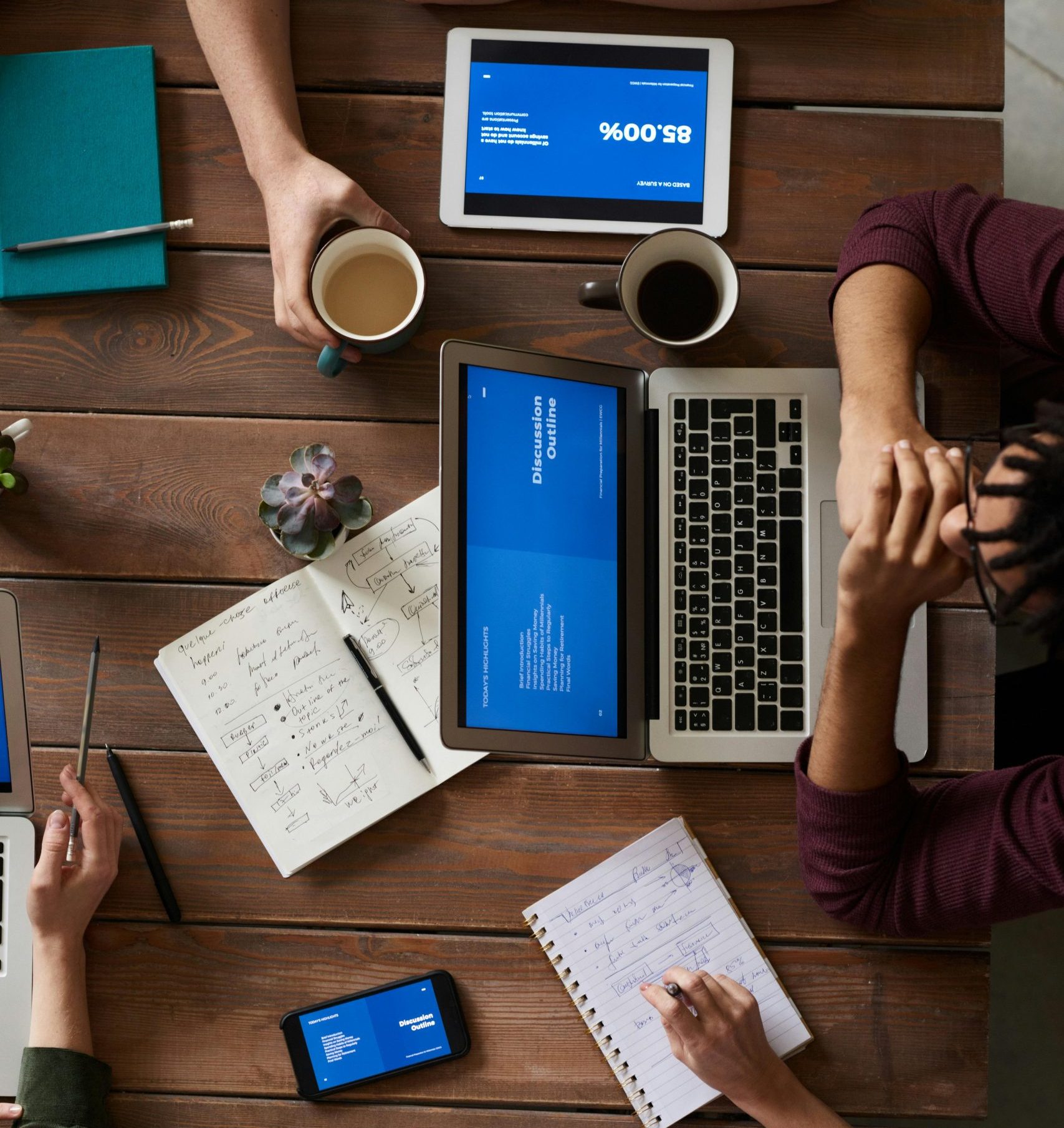 Group of coworkers discussing business strategies with laptops and tablets in a modern office setting.